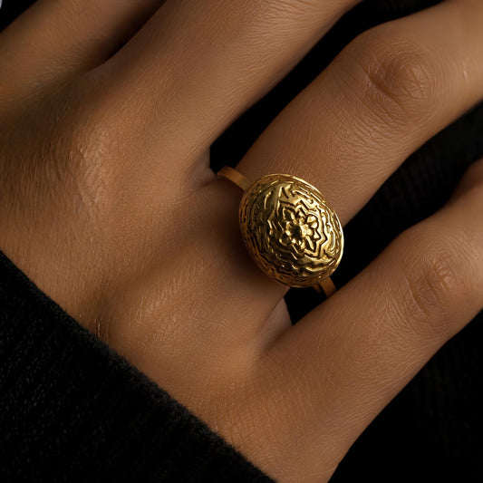 A close-up of a hand wearing a gold plated ring with traditional rosette pattern texturized to decorate a domed solid gold solitaire in a beautiful antique finish. 
