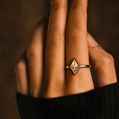 A close-up of a hand wearing gold plated Maktub ring featuring Arabic calligraphy by FABLED set against a dark, warm brown background.