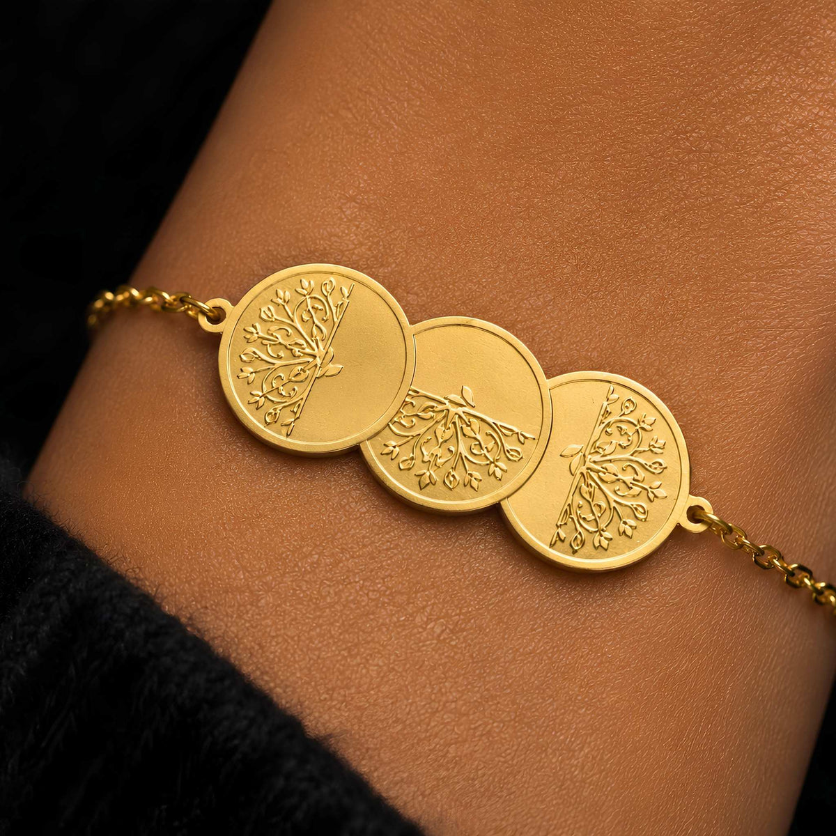 A pattern of rotating plume sprays on a re-imagined traditional layered 3-coin gold bracelet on a person's wrist.