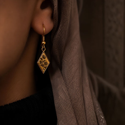 18K gold-plated  minimalist Southeast Asian floral tapestry motif engraved beautifully on delicate diamond shaped earrings worn by a person with a brown headscarf.