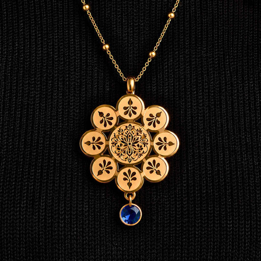 Gold plated necklace with a stylized rosette motif sketched on the parts and petals of a classic floral pendant with a royal sapphire blue dew drop gem. 