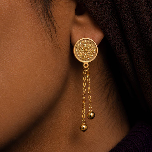 A classic foliage motif scattered design on a traditional gold plated coin earrings worn by a person with a dark background.