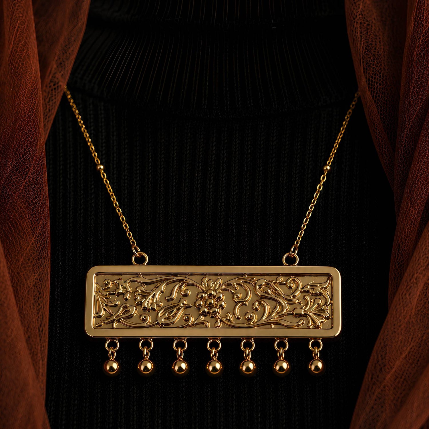 Gold plated necklace with a vintage floral motif framed within a rectangular panel and decorated with a golden fringe of dancing beads on a model.